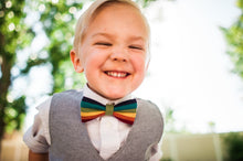 Load image into Gallery viewer, Young child smiling and wearing a rainbow bow tie. Photography by https://www.brianneheiner.com/